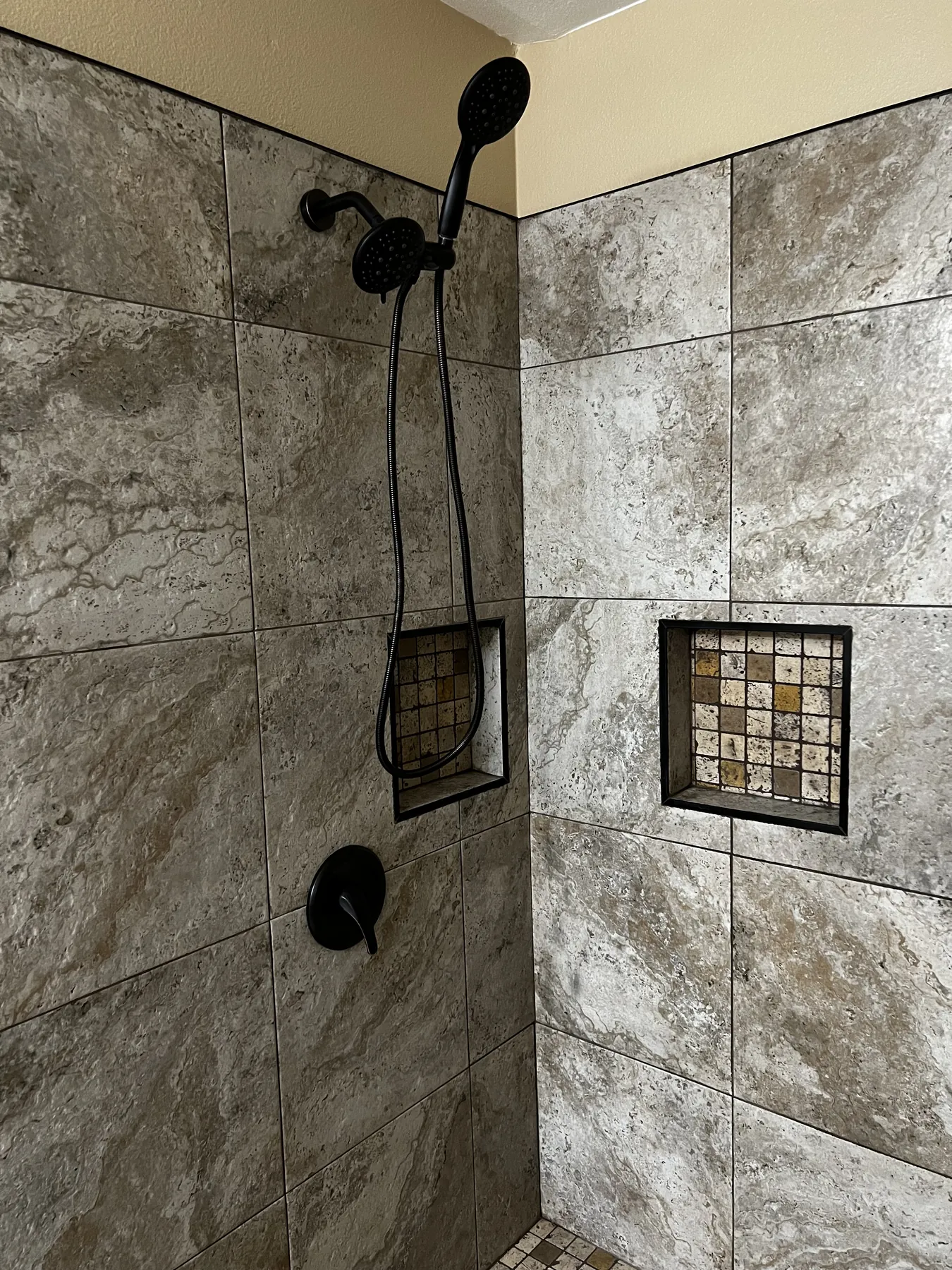 Completed dark tile shower with matte-black fixtures and recessed niches
