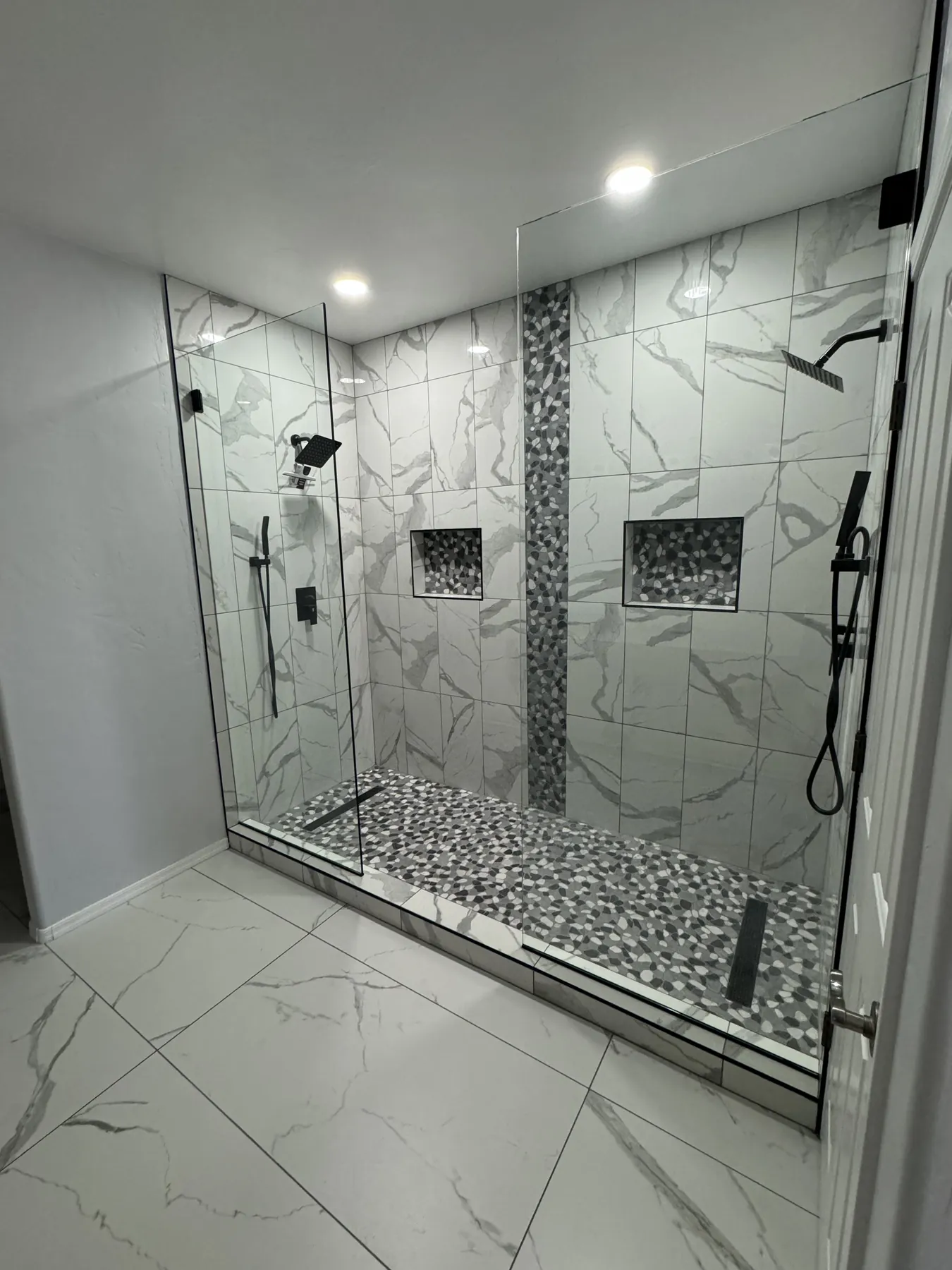 Completed marble-look walk-in shower with glass enclosure and multiple fixtures