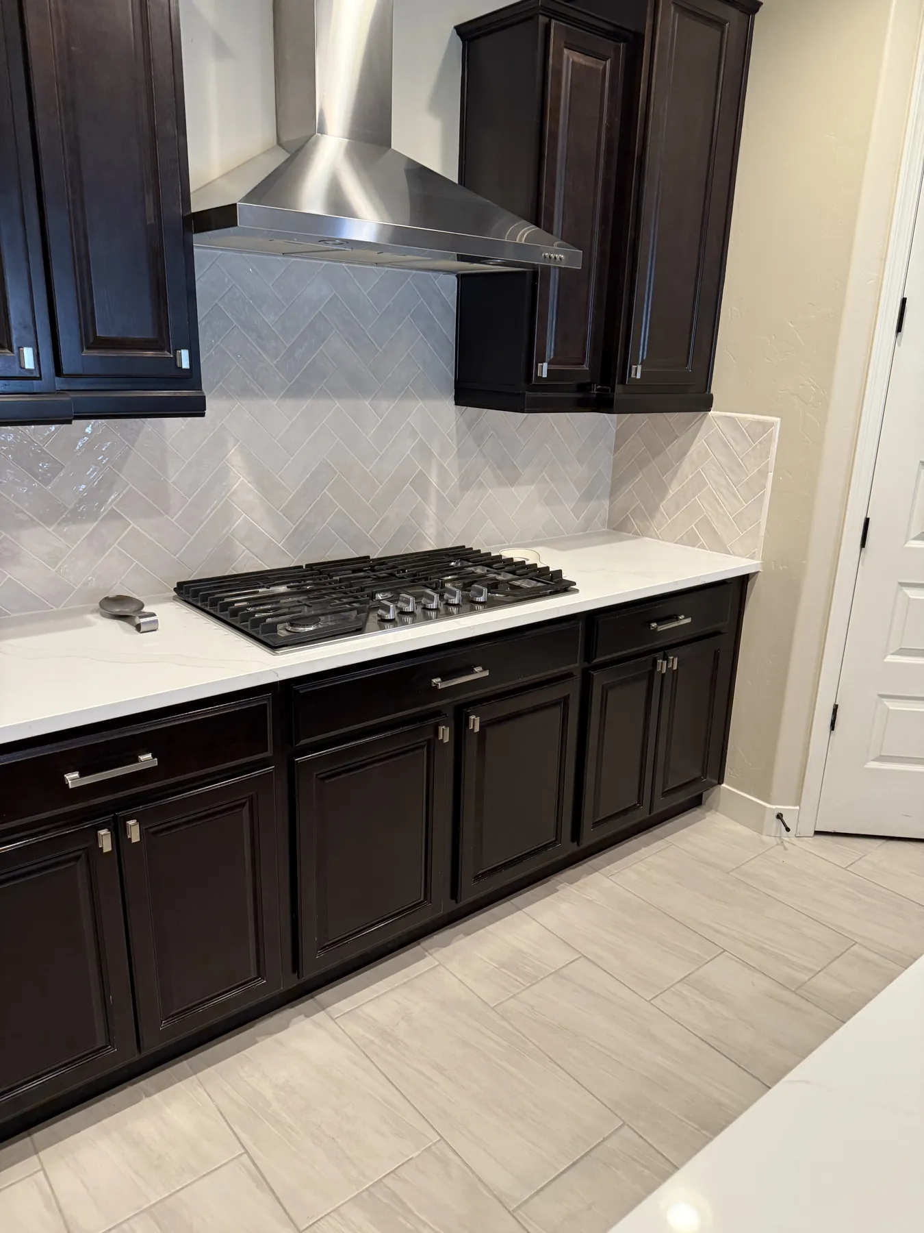 Dark wood kitchen cabinetry with cooktop, hood and backsplash
