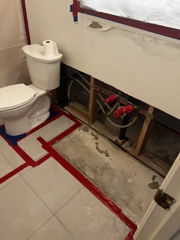 Bathroom wall opened around plumbing with sealed floor protection